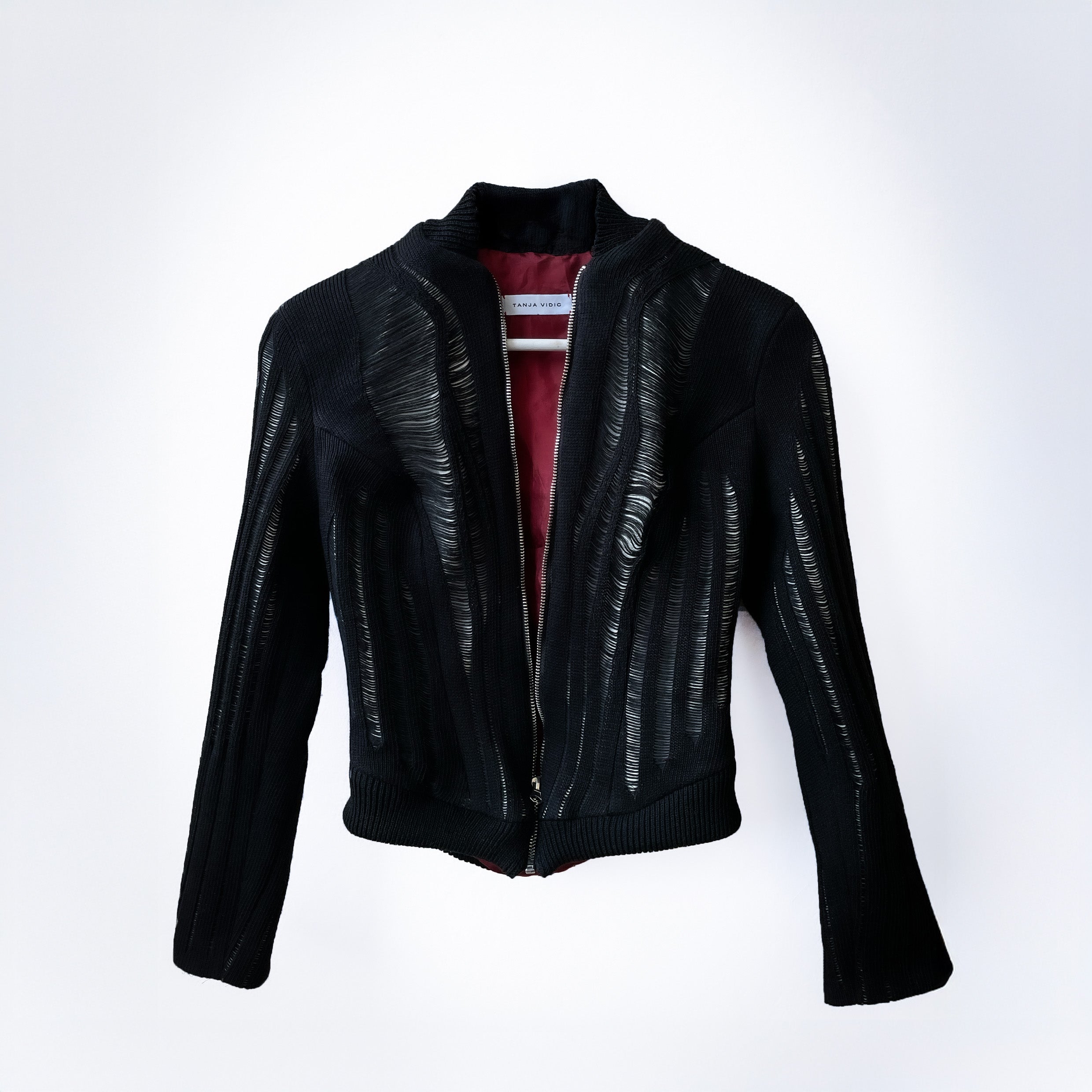 White leather and black knit fitted jacket with red lining on light grey background 