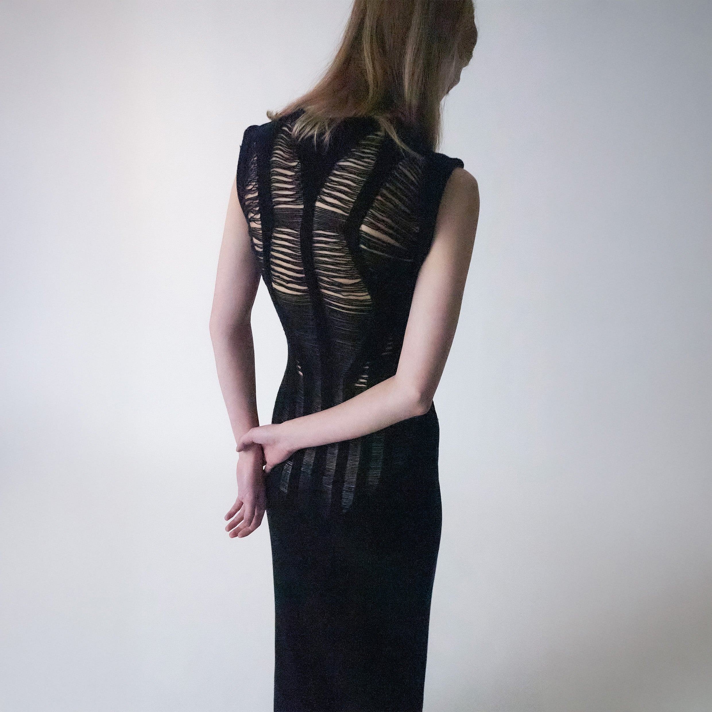 Long black knitted dress with long floats details on a light grey background 