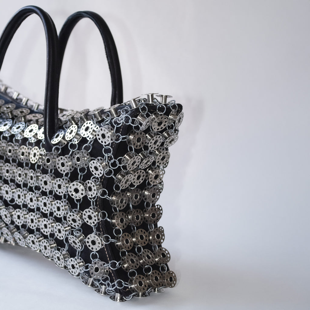 black leather star formed handbag layered with metal bobbins on light gray background 