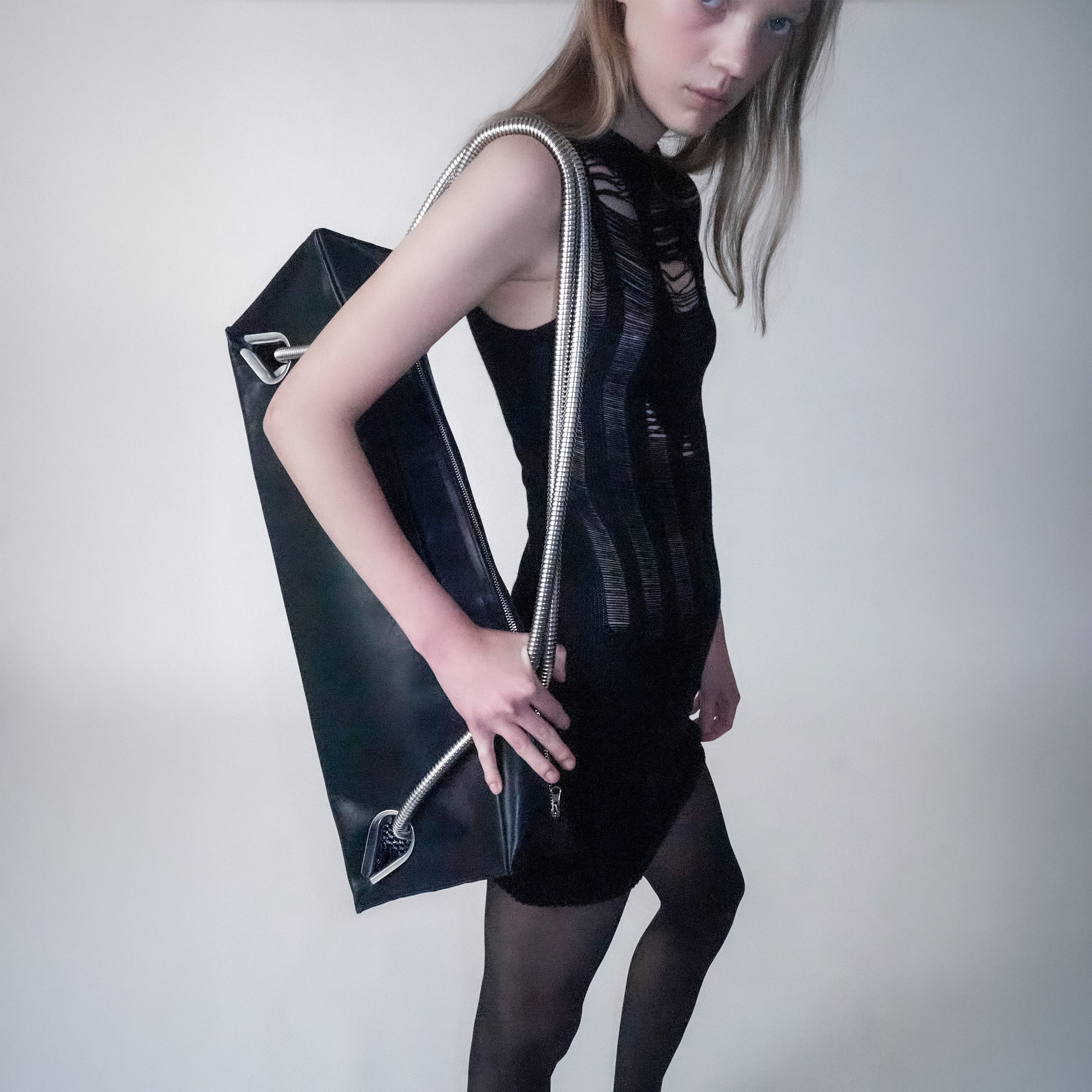 Short black knitted dress with floats on the back and front on a light gray background. the person holds a black leather bag on the shoulder with metal handles 