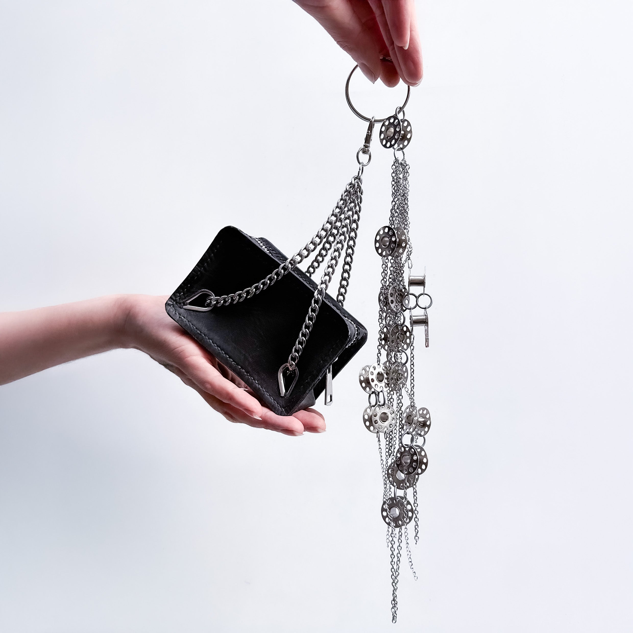 mini black leather bag with metal chain handles as a bag's charm  with a metal-bobbins and metal-chains composition bag's charm on a light gray background