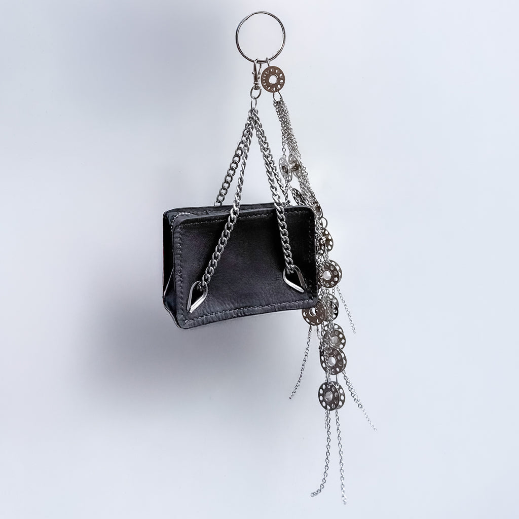 mini black leather bag with metal chain handles as a bag charm  with a decorative keychain with metal bobbins and chains