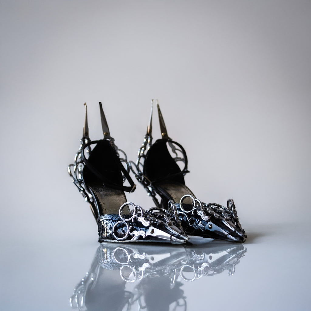 up cycled leather black heels adorned with metal scissors on a light gray background. 